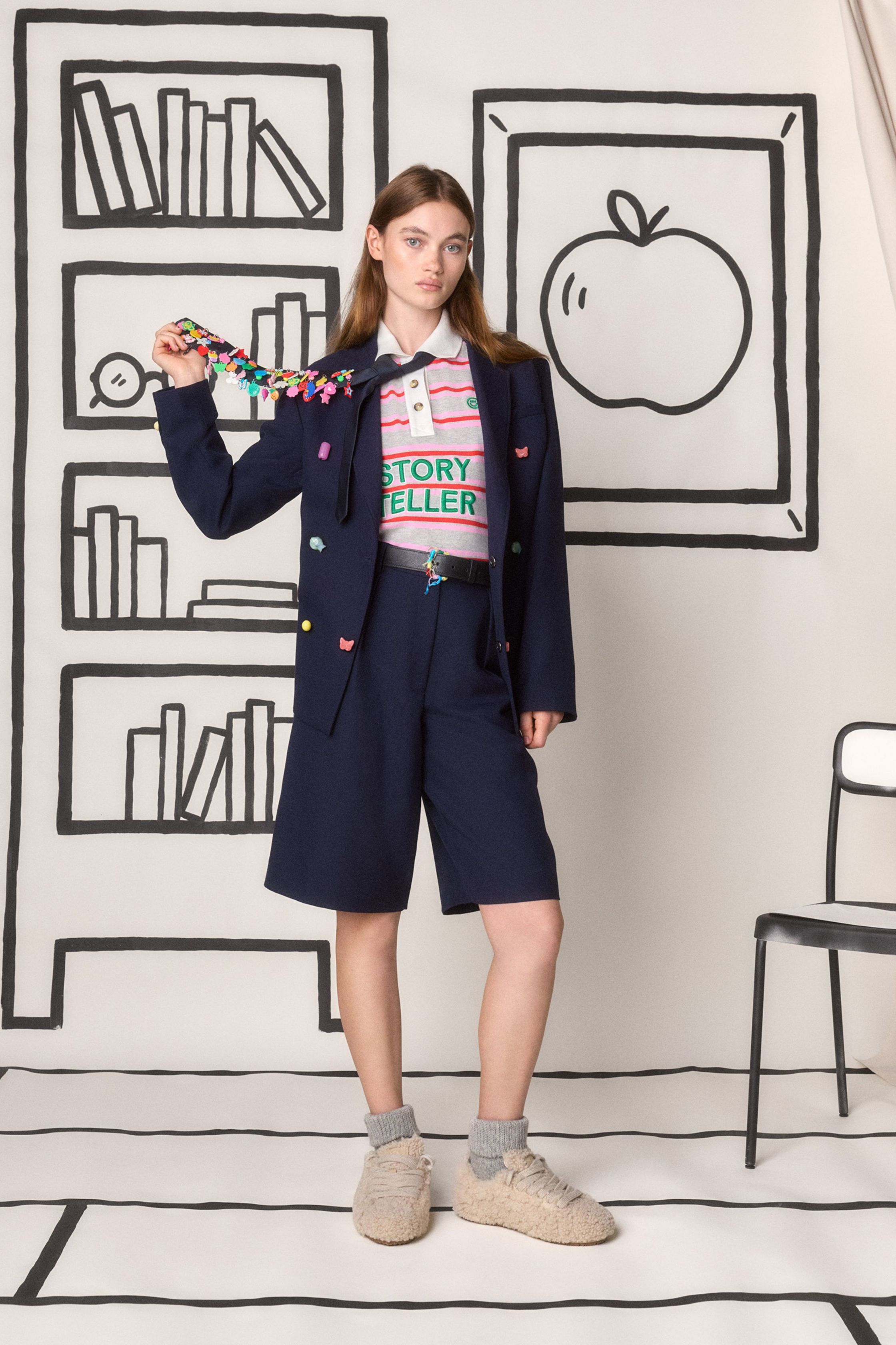 Mira Mikati 本季继续以充满童趣的视觉语言构建一个轻松而充满想象力的衣橱：卡通刺绣、学院领带、彩色针织和宽松半裙构成一个介于校园与艺术工作室之间的世界。鲜亮黄色、菱格针织和手绘背景让整场秀像一本立体绘本，充满快乐与创意-顽石频道趋势研究